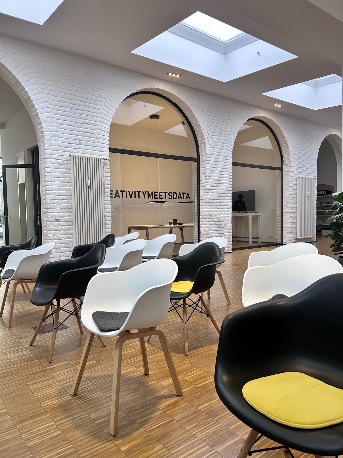 Bestuhlter Seminarbereich bei ONE8Y in Wiesbaden mit schwarzen und weißen Stühlen, Rundbögen und dem Schriftzug Creativity meets Data